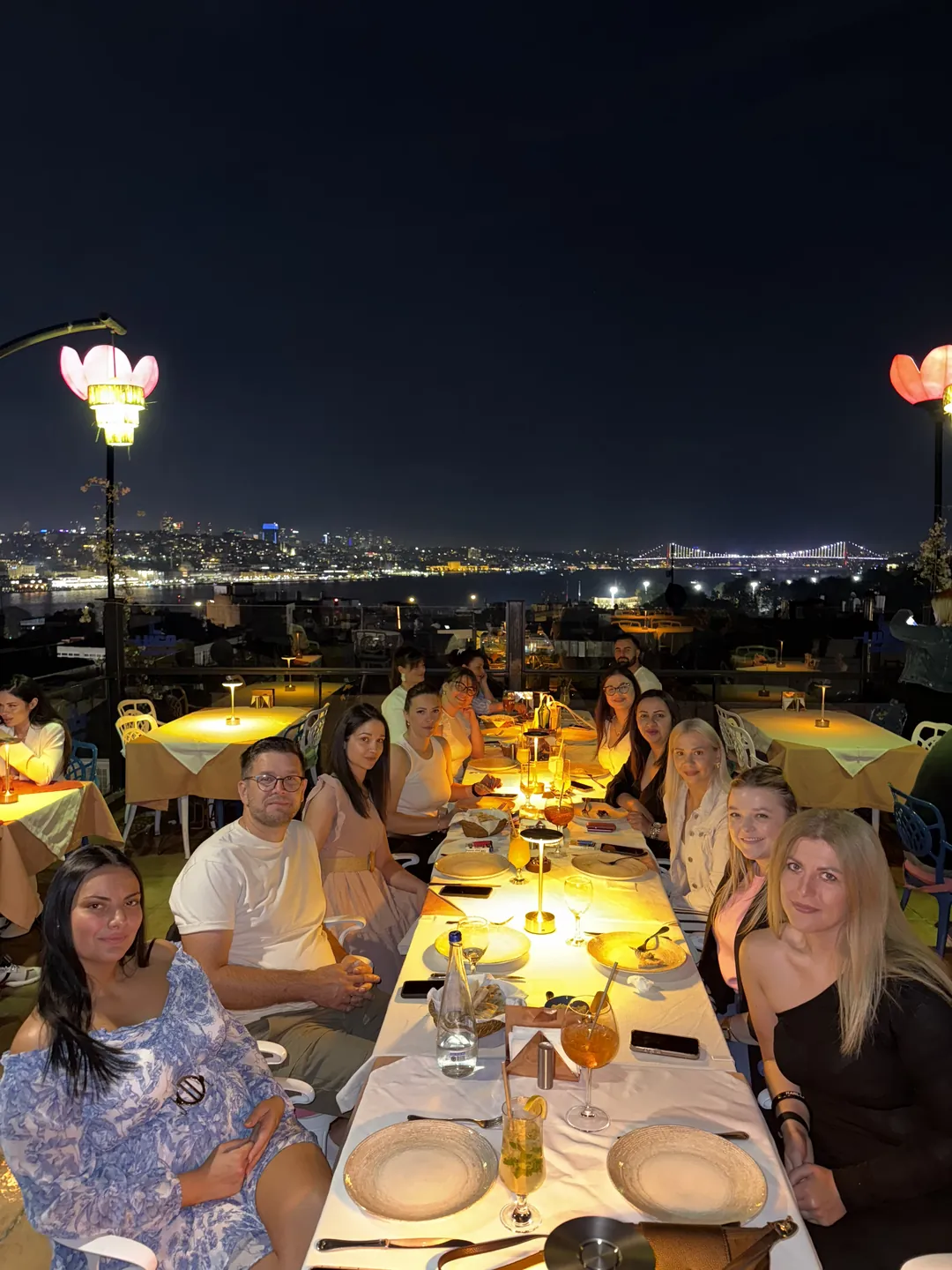 Grupa za stolom na terasi, panorama Bosfora i osvetljen most u pozadini